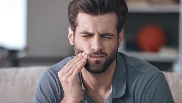 Wincing man holding his cheek in pain
