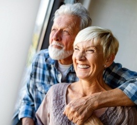 Senior man and woman hugging while looking out window